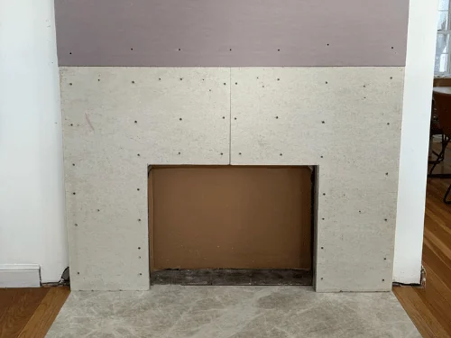 Fireplace surround sheathed in cement board below and purple drywall above, before finishing