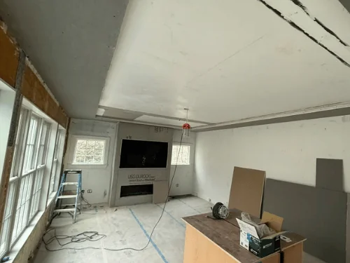 Living room with new drywall going up on the ceiling and soffit, walls open to spray foam insulation