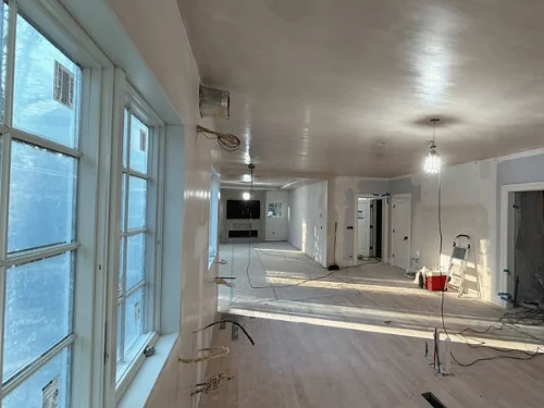 Finished drywall walls and ceiling along a row of windows in a long living room