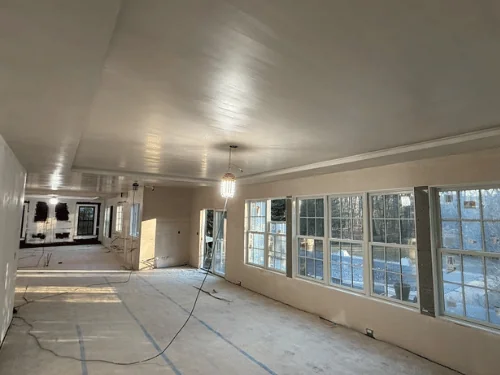 Living room with a finished drywall tray ceiling and walls, sunlight across the protected floor