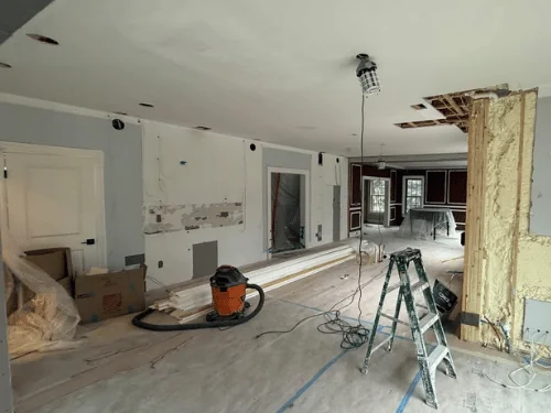 Renovation with patched walls, an opened section showing spray foam and flooring stacked on protection paper