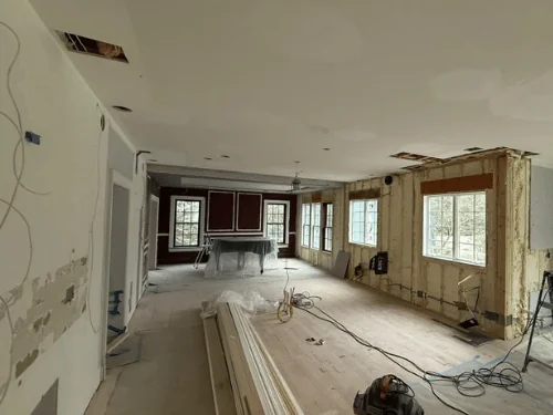 Long room mid-renovation with ceiling and wall patches and trim boards stacked on the floor