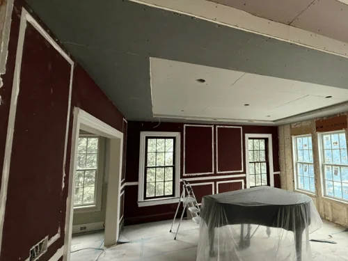 Red-walled room with patched panel outlines, a new drywall ceiling and a piano wrapped in plastic
