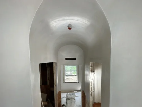 Hallway with a pointed barrel-vault ceiling in smooth plaster, arched openings leading to a window