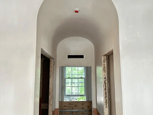 Arched plaster opening framing a hallway that ends at a double-hung window