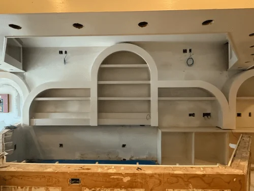 Arched shelf niches finished in white along a bar wall, plywood bar front in the foreground