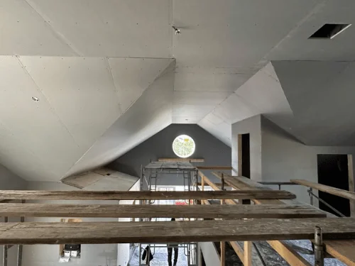 Attic with sloped ceilings hung in blueboard, screw rows visible, and planks set up as a work platform