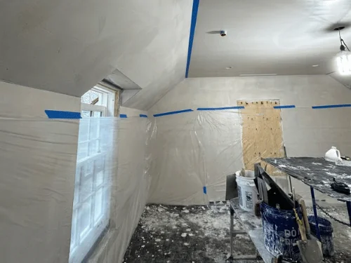 Attic room with plaster on the sloped ceiling, walls masked and tools on a work table