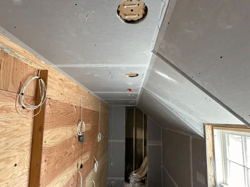 Attic room with sloped ceilings in blueboard and taped joints, one wall sheathed in plywood