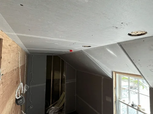 Blueboard ceiling with taped joints meeting a dormer window, plywood on the opposite wall