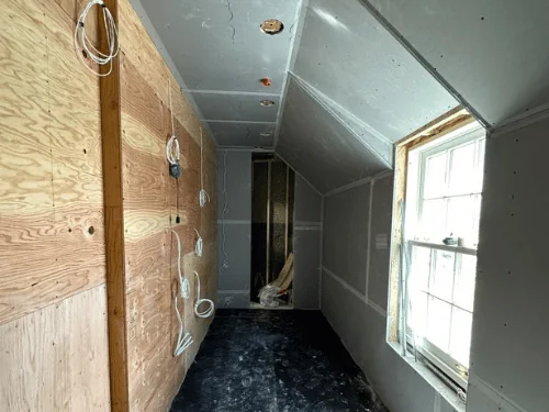Narrow attic room in blueboard with taped seams, sunlight on the protected floor