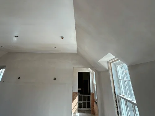 Bright room under sloped ceilings, walls and ceiling in fresh plaster, doorway to the next room
