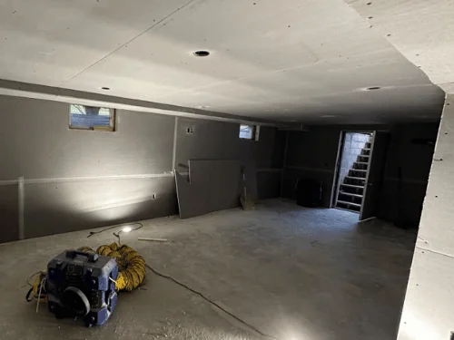 Basement walls in blueboard with taped joints, an air mover and duct set up for drying