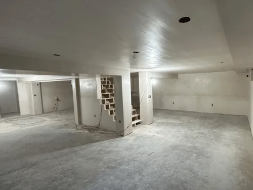 Open basement finished in smooth plaster, the staircase framed in at the back