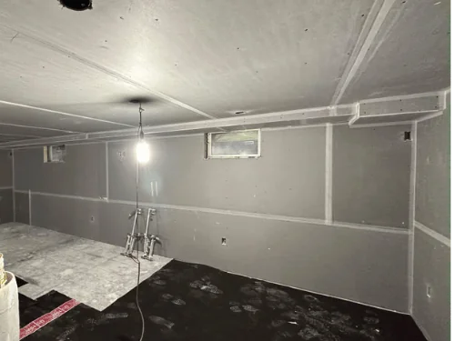Basement bathroom area in blueboard with taped seams and plumbing rough-in at the floor