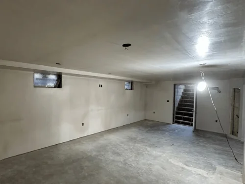 Finished basement with smooth plaster walls, small windows and the bulkhead stairs at the back