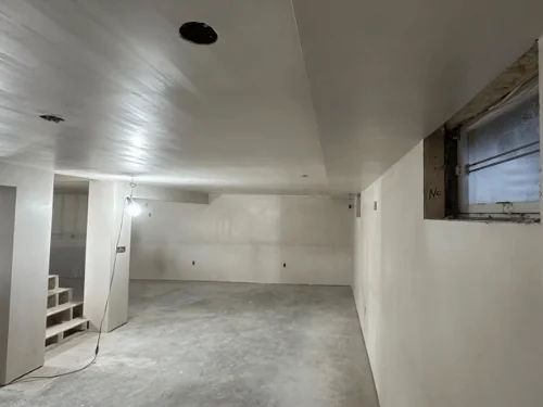 Basement corner with a small window opening and plaster walls running back to the stairs