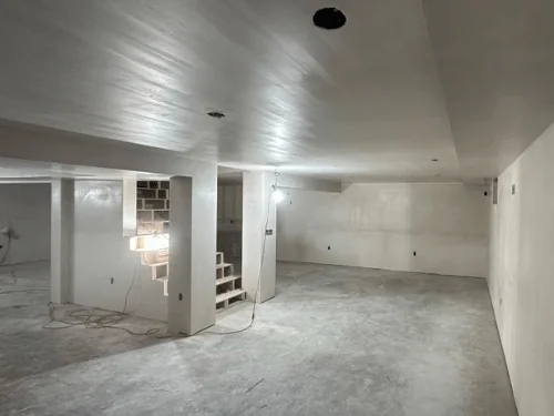 Plastered basement with a soffit along the ceiling and the stair framed in at the back