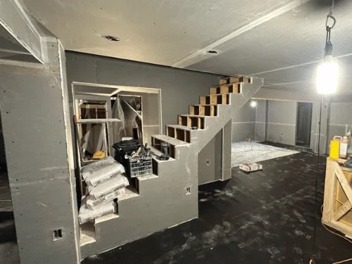 Basement stair wall in blueboard with bags of plaster stacked in the under-stair nook