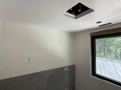 Bathroom with white plaster above a gray tile-backer wall, a window and an exhaust fan opening