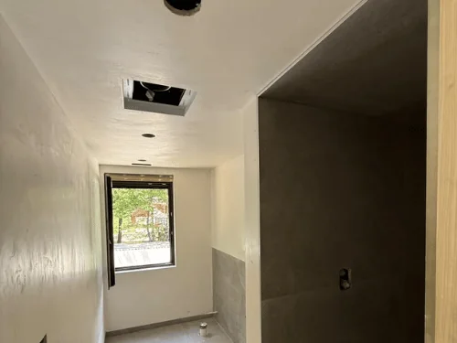 Narrow bathroom with white plaster walls, a dark tile-backer shower wall and a small window