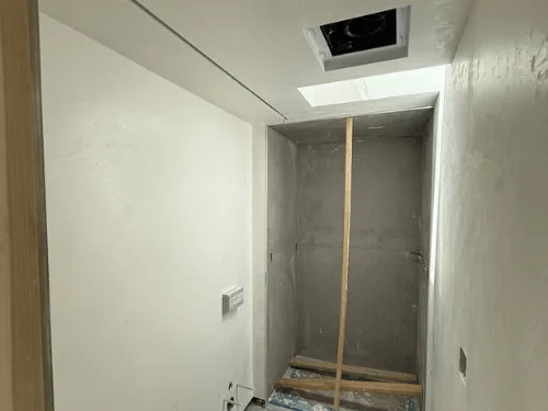 Bathroom with white plaster walls around a gray tile-backer shower alcove, a skylight above