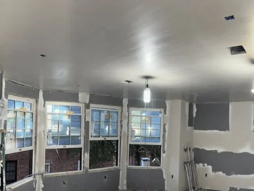 Bay-window room with the ceiling plastered and the blueboard walls taped and spotted