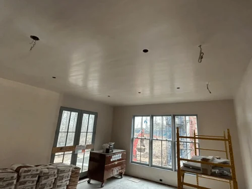 Room mid-project with stacked bags of plaster, a rolling scaffold and a job box against finished walls