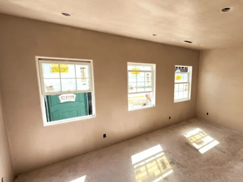 Bedroom with three windows and sunlight on the floor, walls and ceiling in fresh plaster