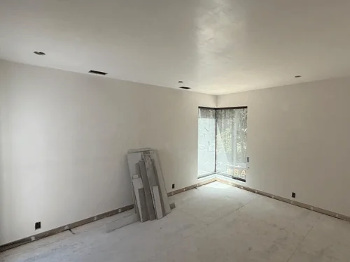Bedroom in white plaster with a corner window and flooring stacked by the wall