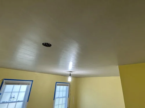 Freshly plastered ceiling over a room with existing yellow walls, windows masked with tape