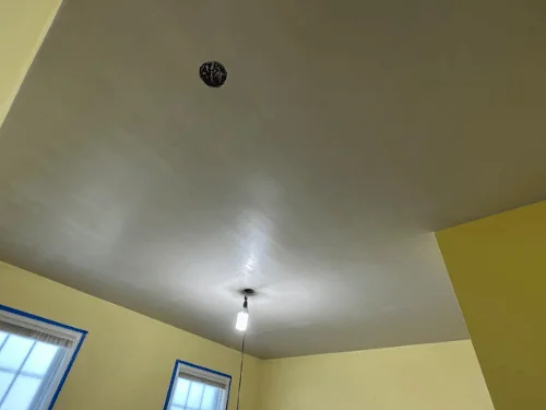 New plaster ceiling meeting existing yellow walls, light fixture box in the center