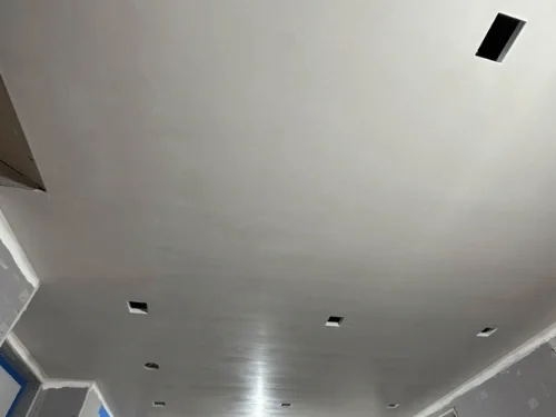 Wide plastered ceiling with cutouts for recessed lights, walls still in board below