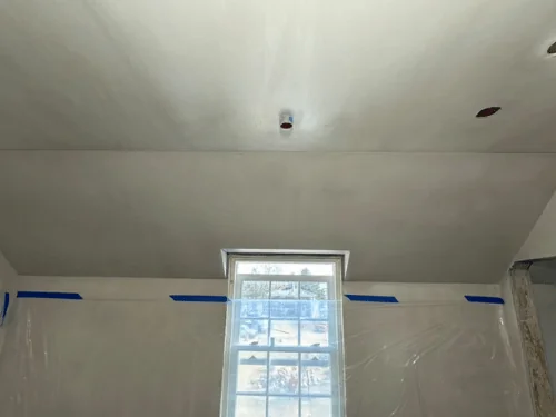 Room masked with plastic below a blue tape line, the ceiling and upper walls freshly plastered