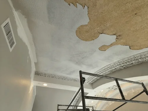 Old ceiling finish being stripped and skimmed beside ornamental plaster arches, a scaffold in the room