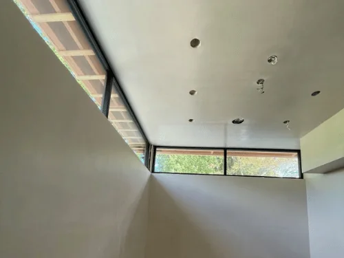 Plastered ceiling meeting a run of clerestory windows, recessed light openings cut in