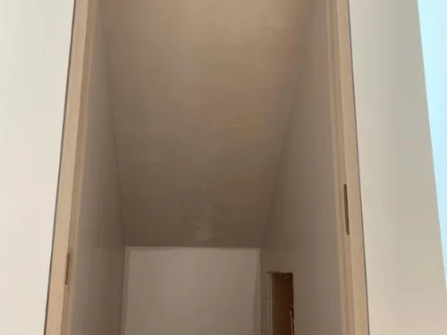 Closet under a sloped ceiling with walls and ceiling finished in plaster
