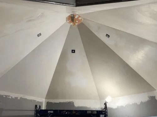 Faceted cone ceiling finished in plaster above blueboard walls, with a scaffold in the room