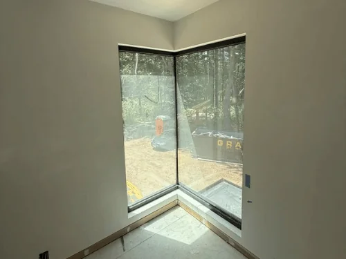 Glass corner window set into white plaster walls, sunlight across the floor