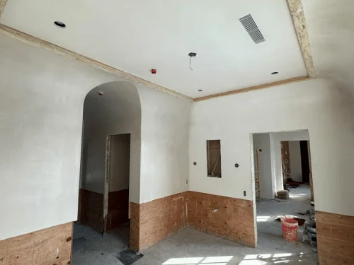 Room with a coved plaster ceiling and an arched doorway, plywood wainscot backing along the base