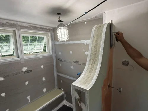 Curved shower half-wall being built out, flexible corner bead on the edge and board seams patched