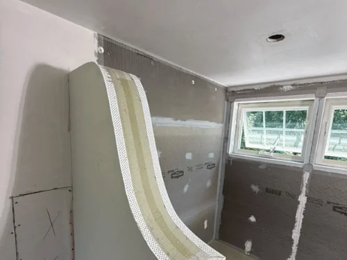 Curved half-wall with flexible corner bead and patched board behind it, before the finish coat
