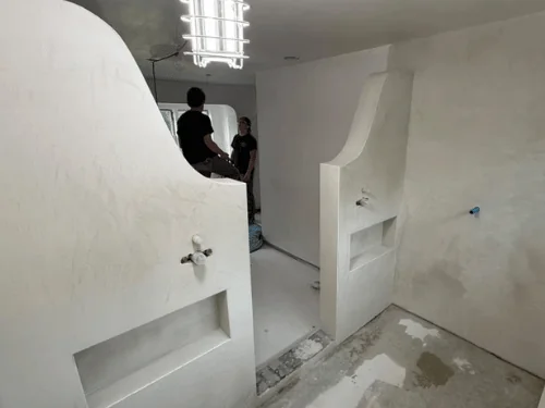 Finished curved half-walls with recessed niches in a bathroom, crew working in the background