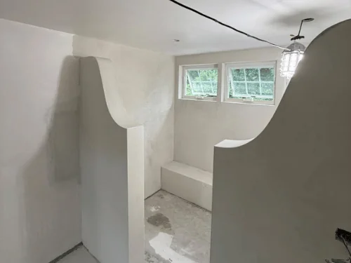 Pair of curved plaster half-walls framing a built-in bench under a row of windows
