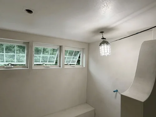 Curved plaster wall sweeping down to a built-in bench beneath three awning windows
