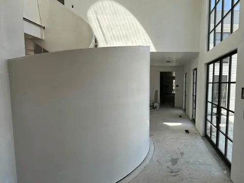 Tall curved plaster wall wrapping a spiral stair beside a wall of steel windows