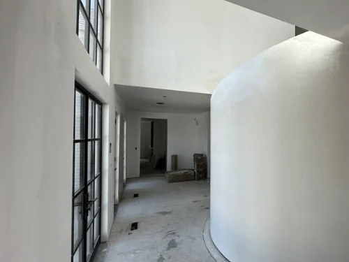 Curved plaster wall along a hallway lit by tall steel-framed windows