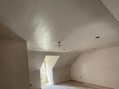 Attic room with sloped ceilings and a dormer window, finished in smooth plaster