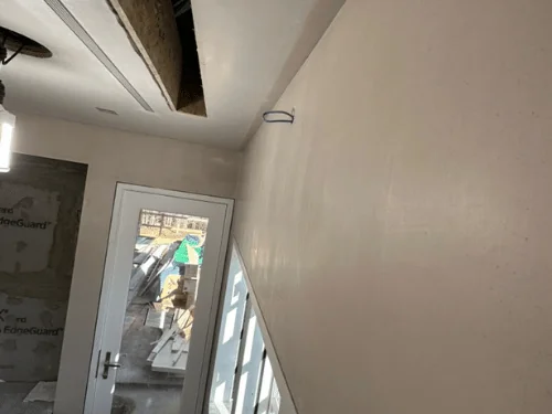 Entry wall finished in smooth plaster beside a glass door, with a ceiling bay still open above