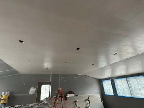 Large room with the ceiling plastered and the walls still in blueboard, stilts and a scaffold set up